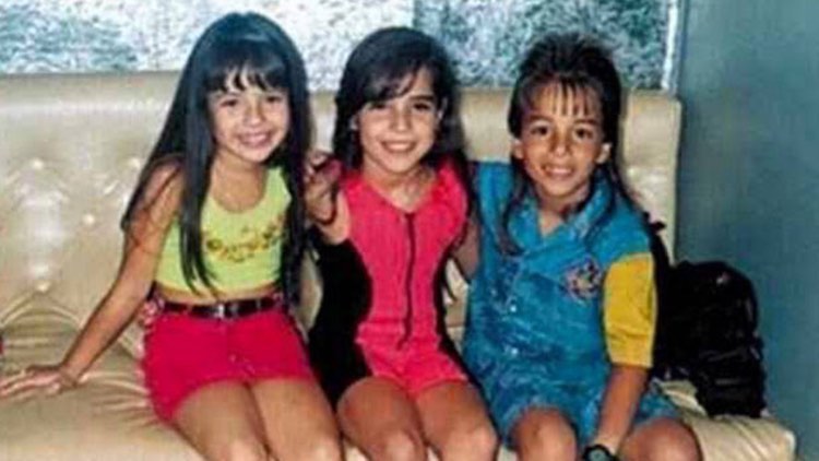 Sandy, Wanessa Camargo e Junior sentados em um sofá posando para fotos ainda crianças