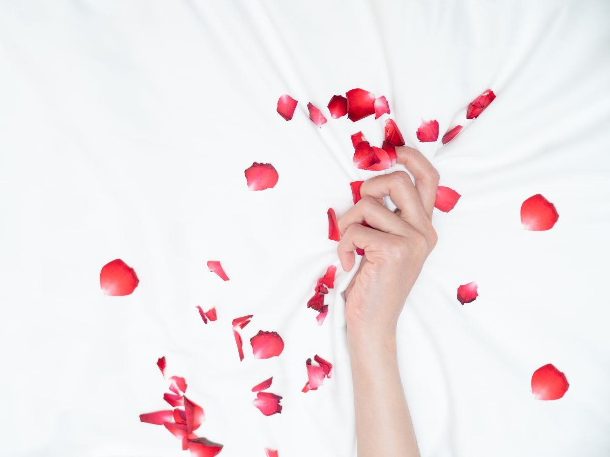 mão de mulher segurando lençol branco onde há várias pétalas de rosa vermelhas, desejo sexual feminino