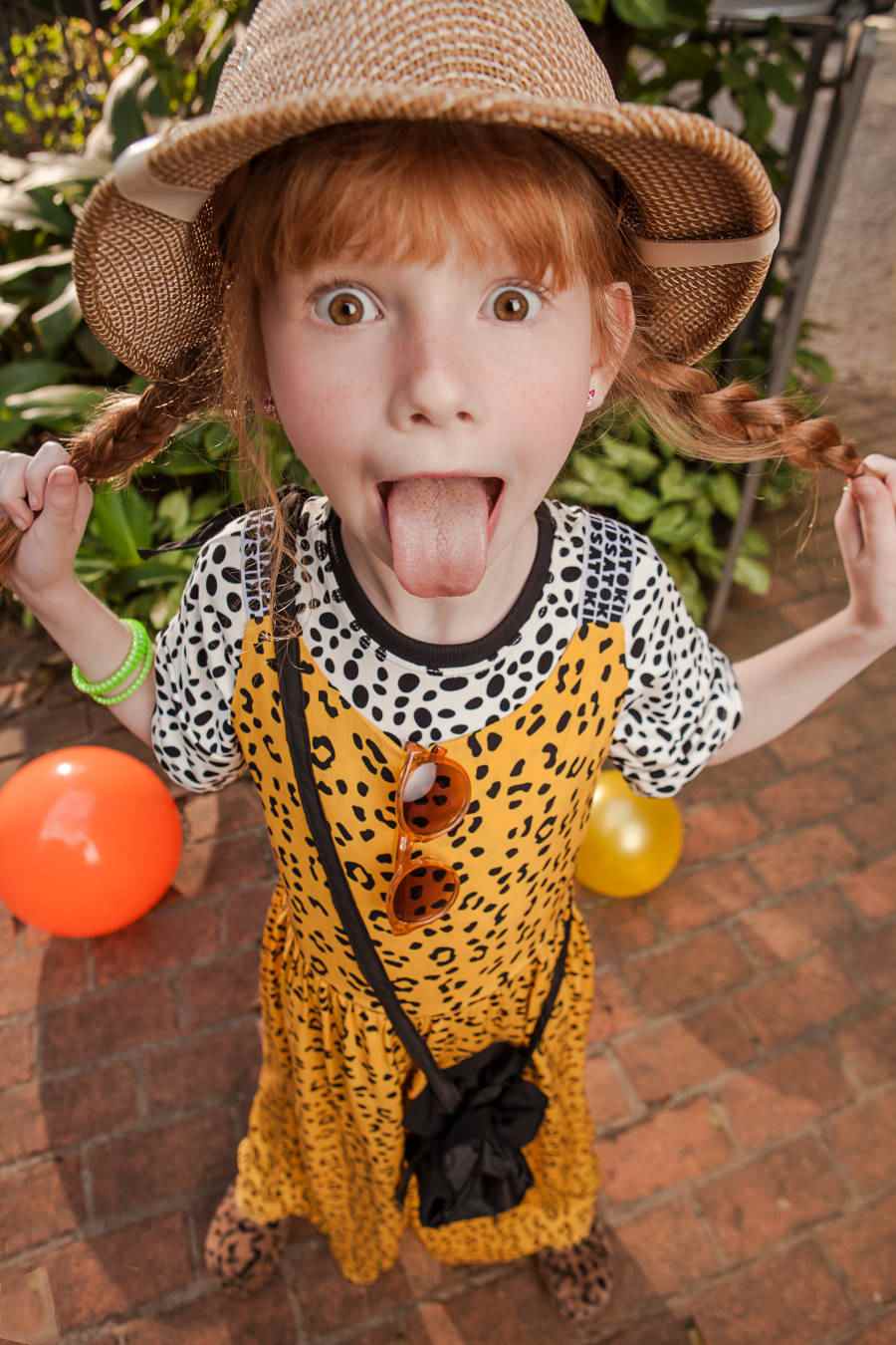 Criança com cabelo com duas tranças e franjas, com a língua para fora e roupa com um mix de estampas animal print e bolsa preta da nova coleção da Sato Kid