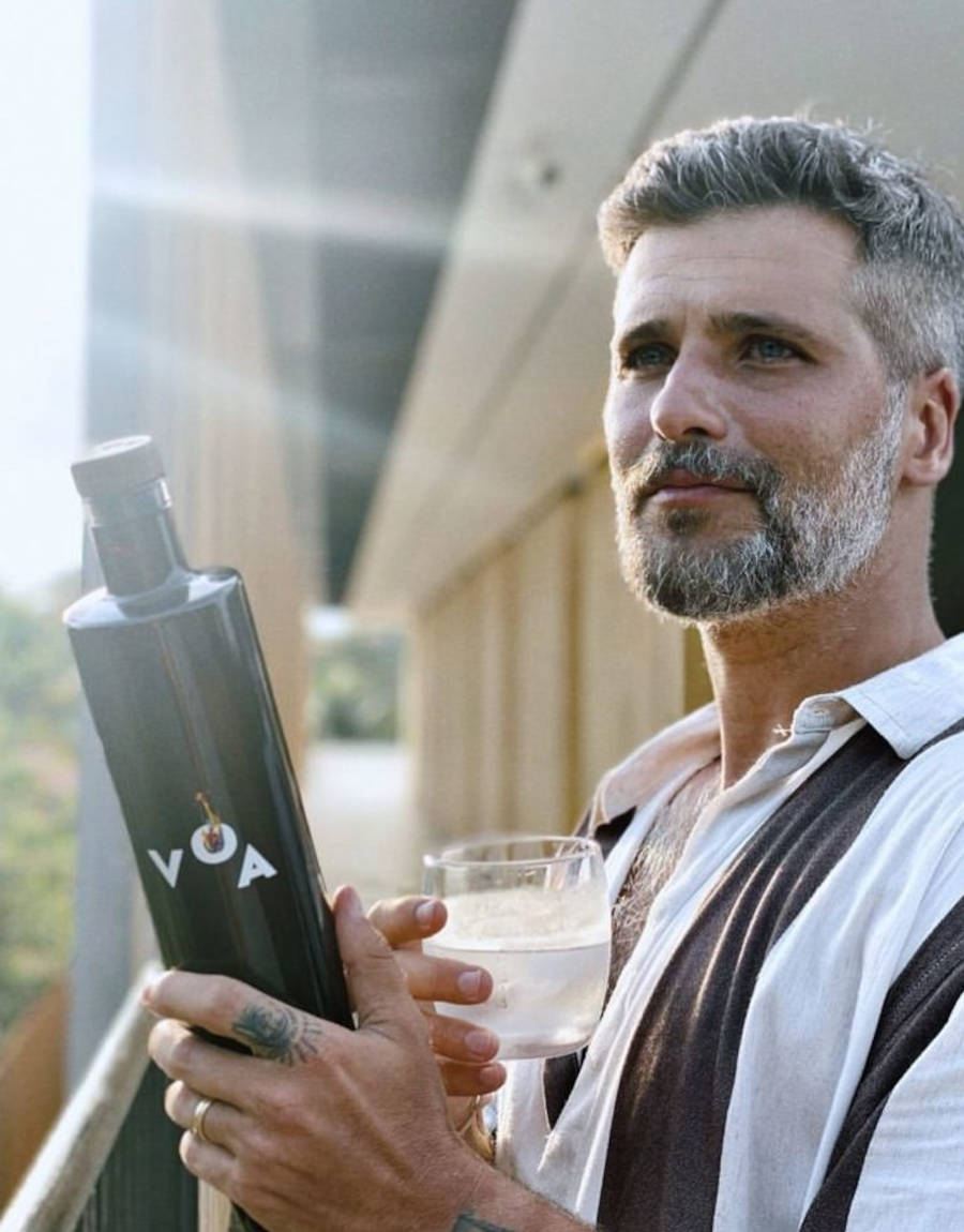 Foto de Bruno Gagliasso segurando um garrafa de vodka Voa e um copo