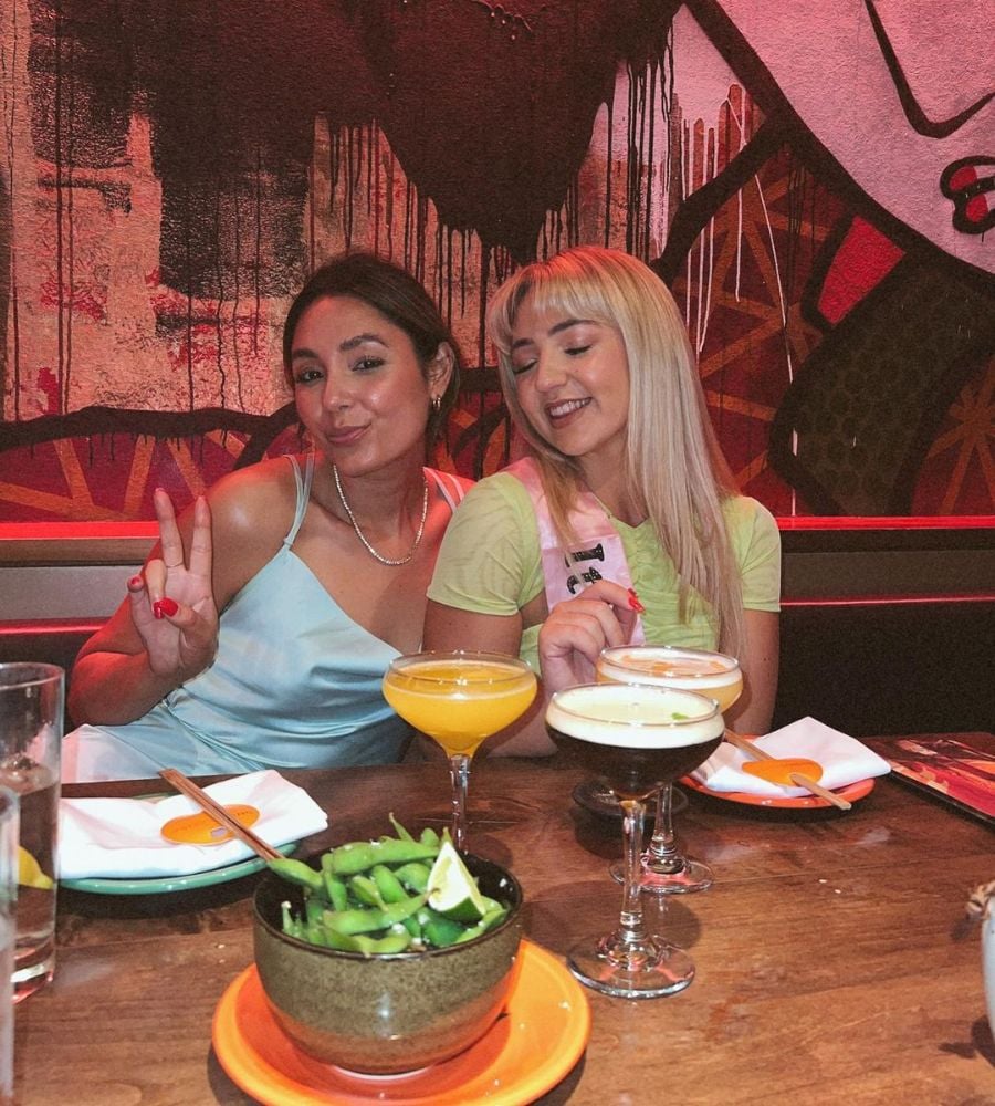 duas amigas sentadas à mesa de um restaurante com taças de marguerita e pratos de comida