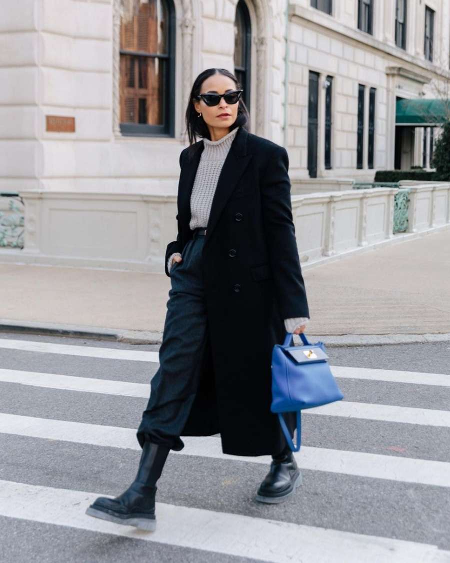 mulher com tricô cinza, calça, sobretudo e bota pretos andando na rua