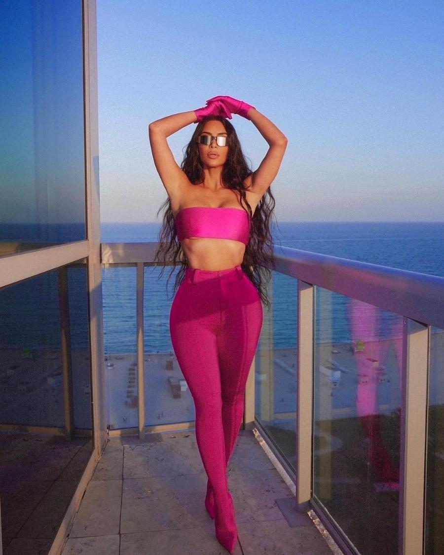 Kim Kardashian usando óculos escuros, luva, top faixa e calça de cintura alta, look all pink