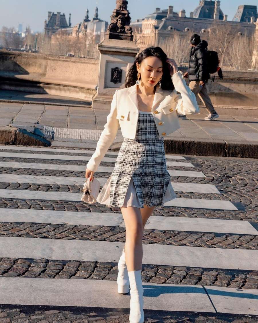 mulher com vestido xadrez, blazer cropped creme e bota branca