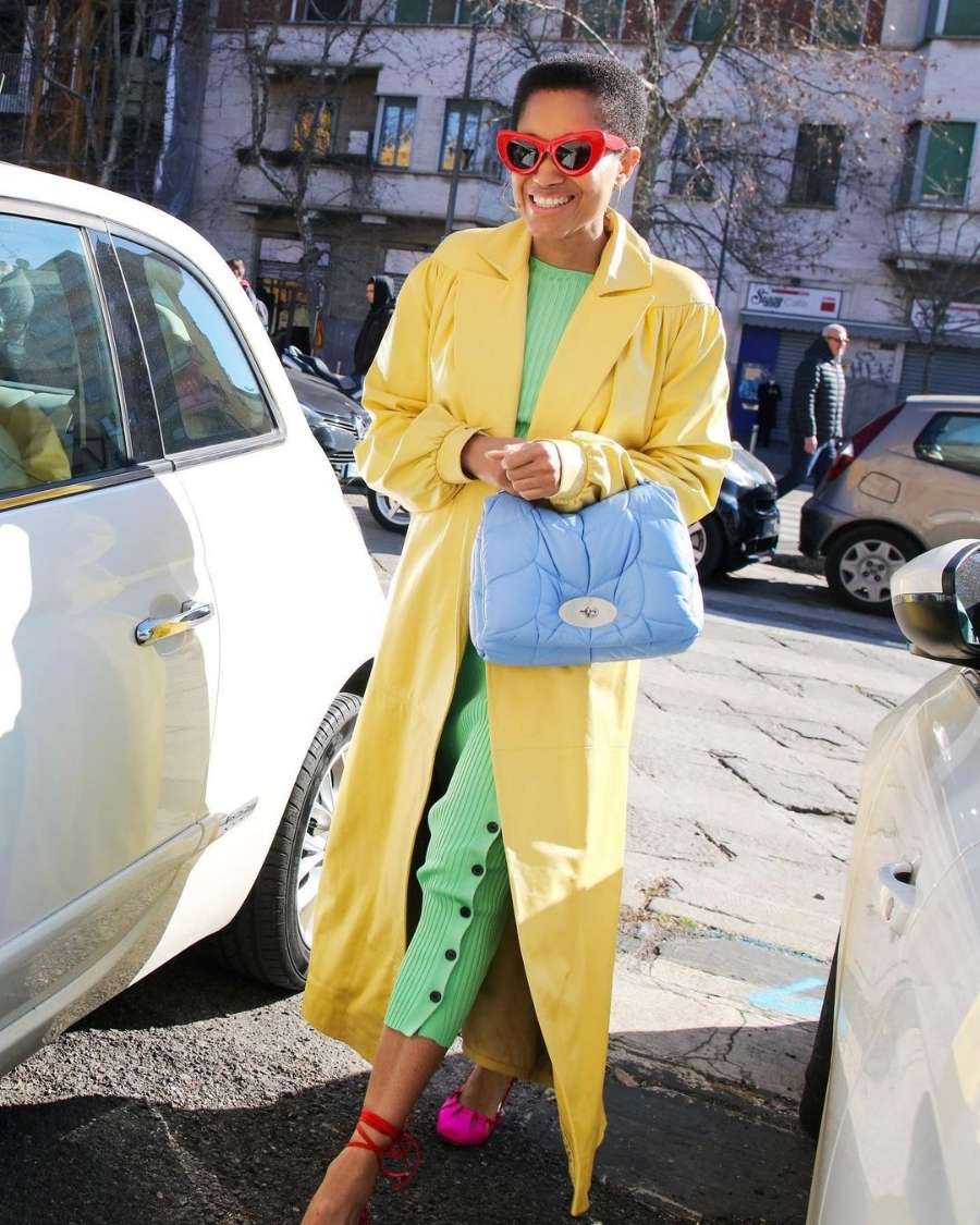 mulher com macacão verde menta, bolsa azul claro e sobretudo amarelo