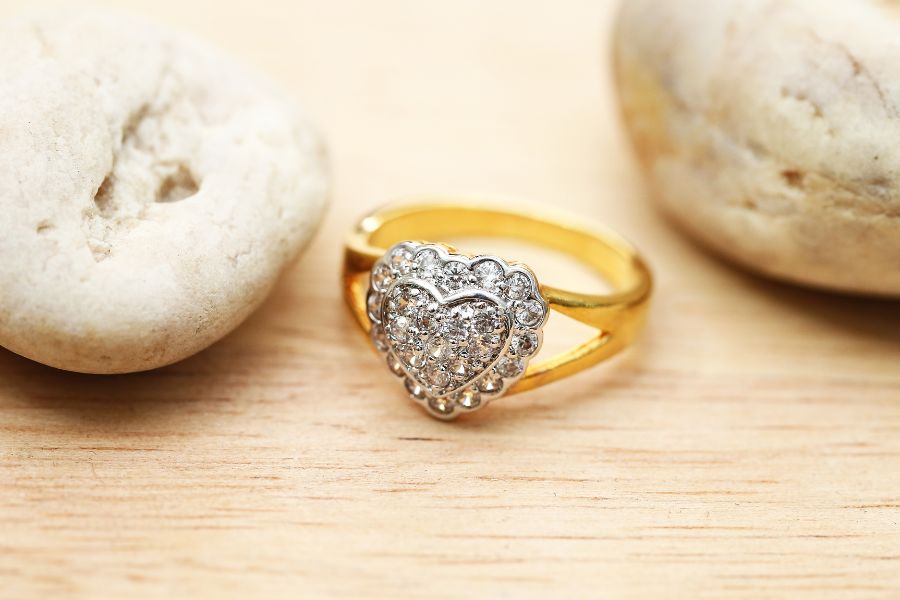 Anel de ouro com duas argolas e coração em mesa de madeira ao lado de duas pedras
