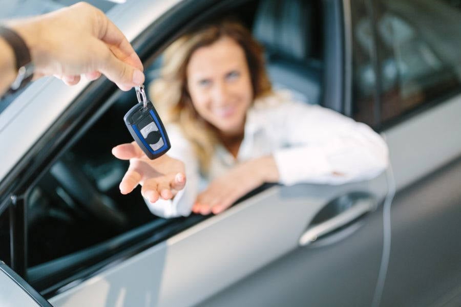 Foto de pessoa segurando chave do carro em evidência, ao fundo, a imagem borrada de uma mulher recebendo a chave