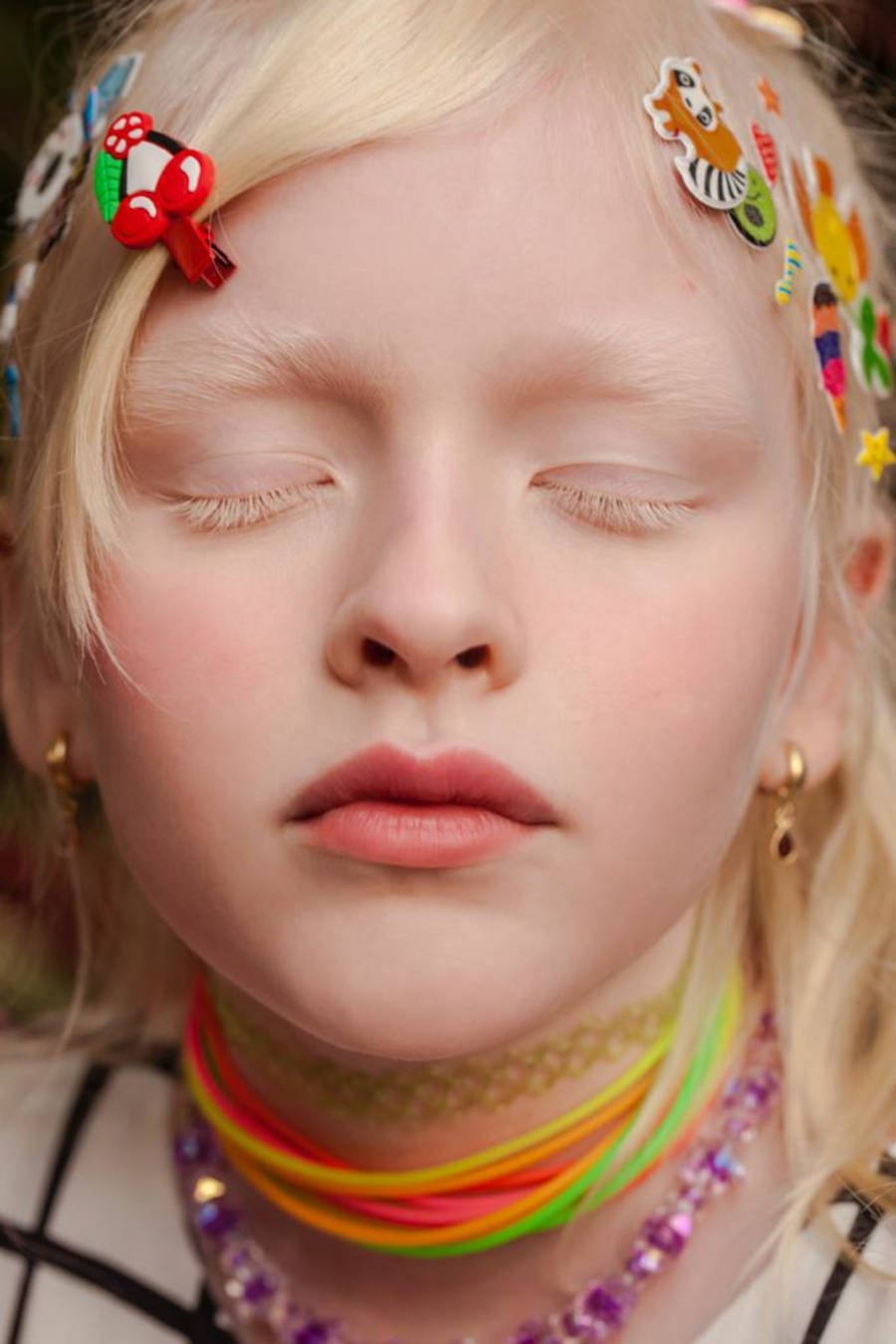 Imagem aproximada do rosto de uma criança loira com stickers no cabelo e colares coloridos