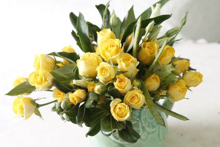arranjo de rosas amarelas com folhagens em vaso de cerâmica turquesa