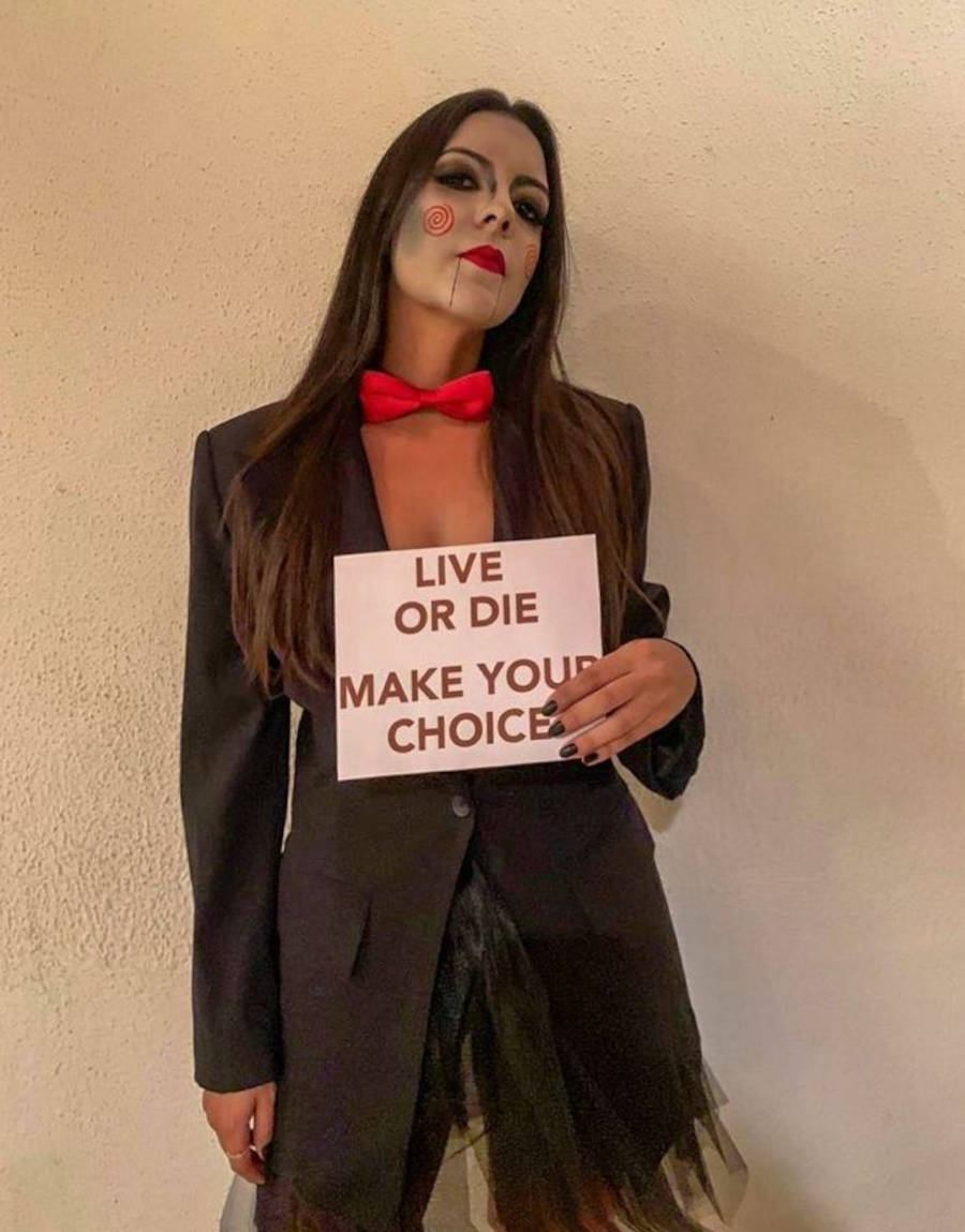 Foto de uma menina com a fantasia do Boneco Saw, segurando uma placa escrito "Live or Die. Make your choice."