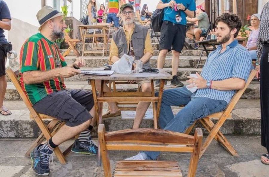 Foto de Chay Suede, Marcos Caruso e Mauro Mendonça Filho sentados em uma mesa de bar para as gravações de Travessia