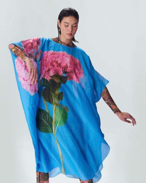 Foto de uma mulher se movimentando com um vestido azul com um ramo de flores rosas