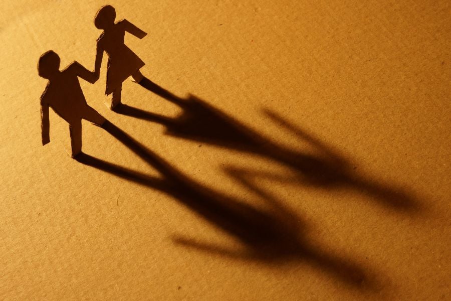 bonecos de papelão de homem e mulher de mãos dadas, projetando sombra sobre uma superfície de papelão