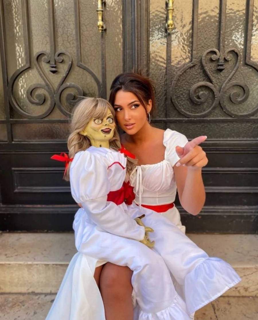 Foto de mulher fantasiada de Annabelle e segurando uma réplica da boneca do filme