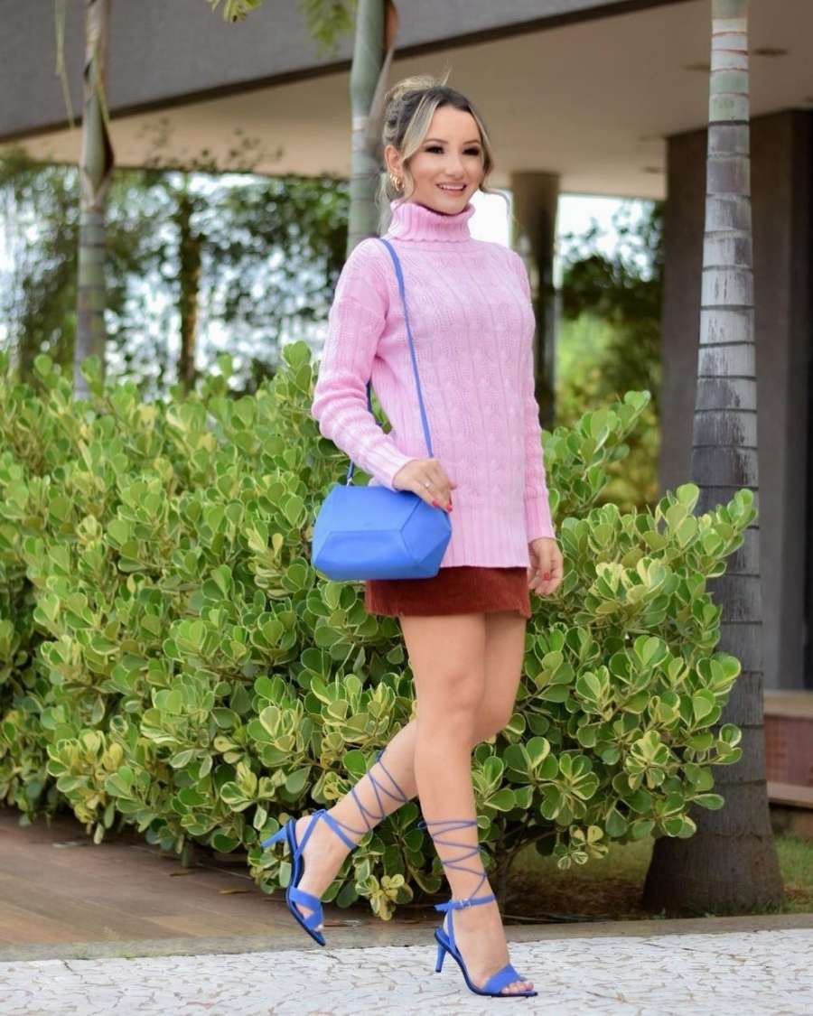 mulher com tricô rosa, saia marrom, bolsa e sapatos azuis