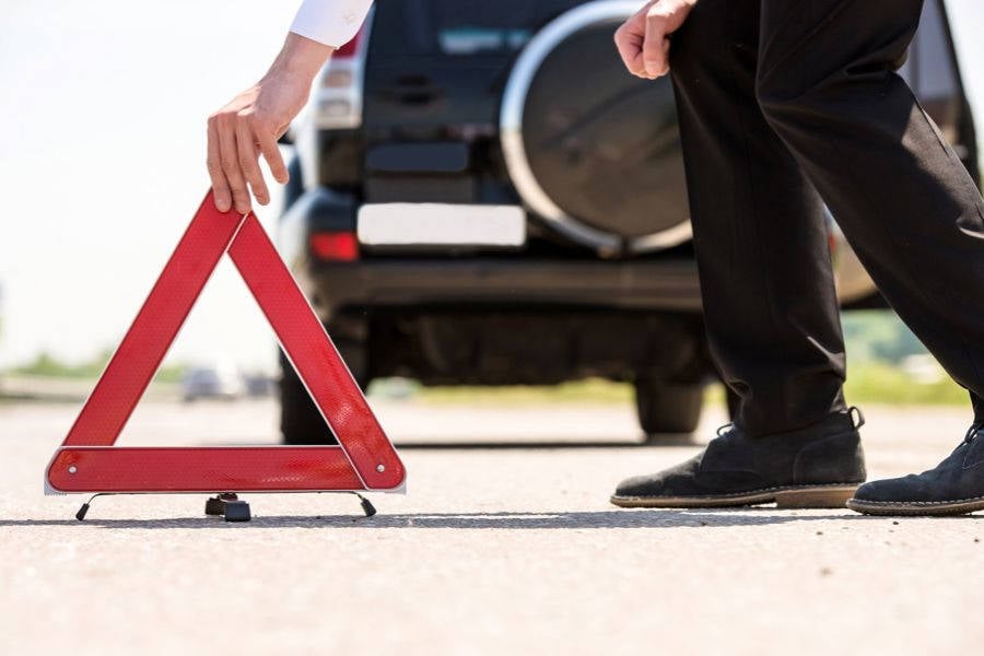Homem com o carro quebrado coloca cone vermelho no asfalto