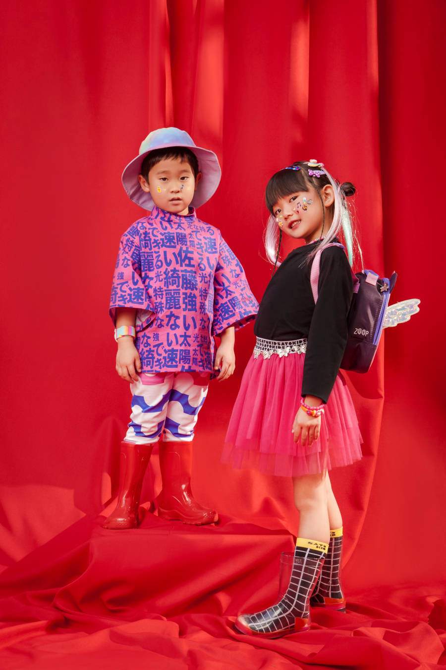 Foto de duas crianças asiáticas na campanha da marca da Sabrina Sato. O fundo da imagem é vermelho