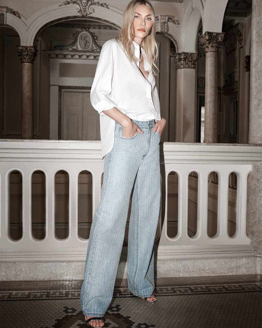 Foto de modelo posando com blusa social branca e calça jeans metalizada