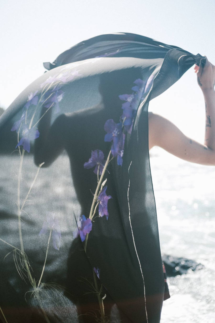 Foto de mulher segurando um lenço preto com flores roxas da Osklen