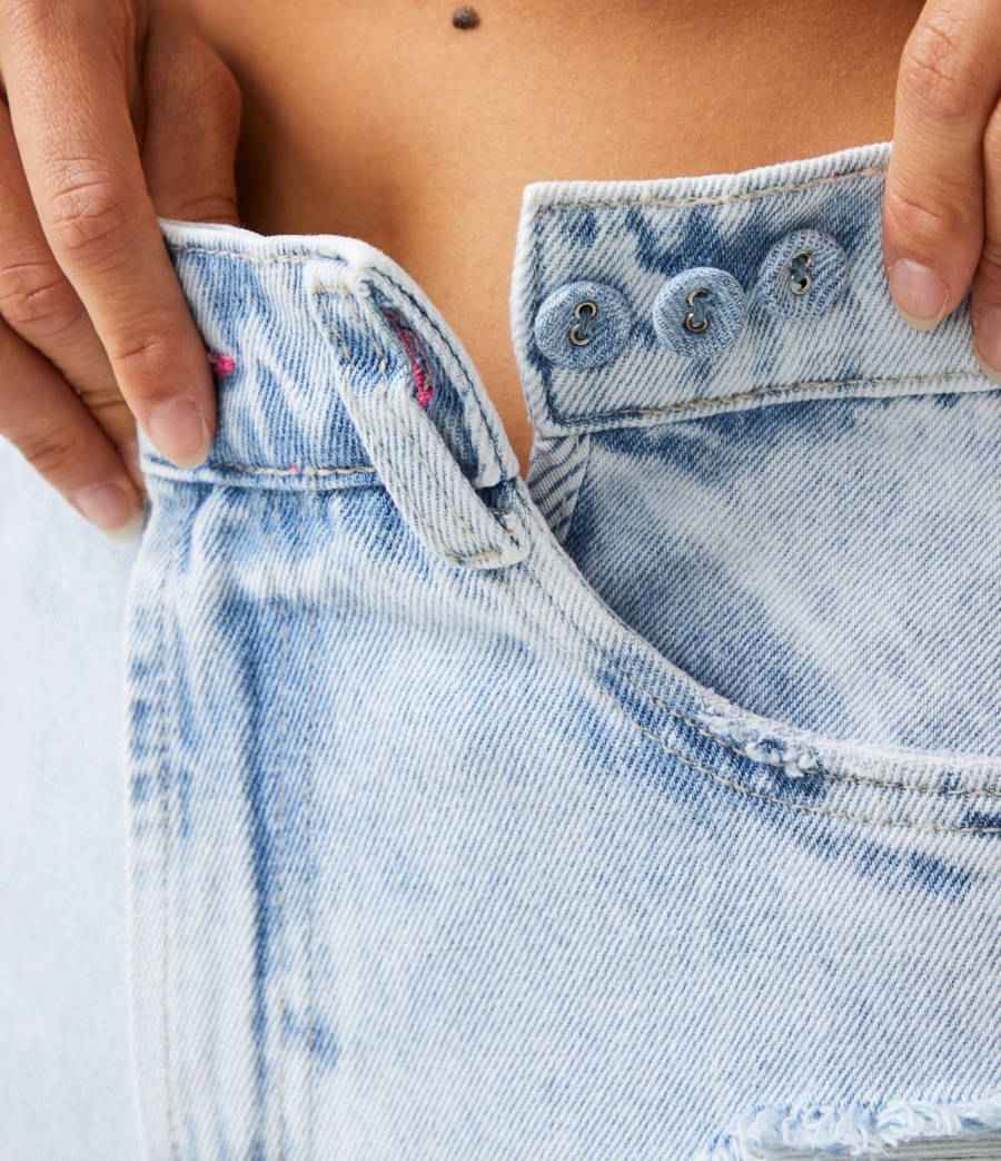 Múltiplos botões em uma calça jeans. Foto com uma mulher fechando os botões da calça