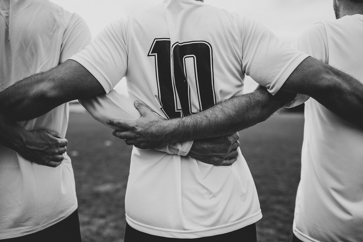 Homens abraçados entrelaçando as mãos uns nas costas do outro e no centro uma camisa de futebol com o número 10 inscrito