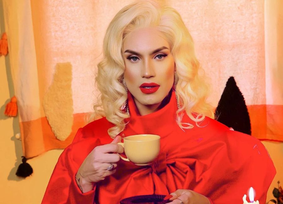 A drag queen Aretuza Lovi com uma roupa vermelha e segurando uma xícara de chá. Ela faz parte da enquete RuPaul's Drag Race