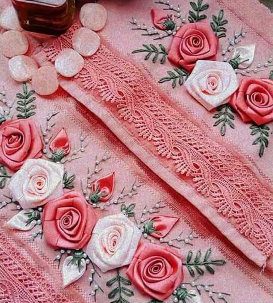 Foto toalha rosa com acabamento artesanal bordado de rosas e botões de rosas em cetim. Peça está sobre superfície e ao lado de pedras brancas.