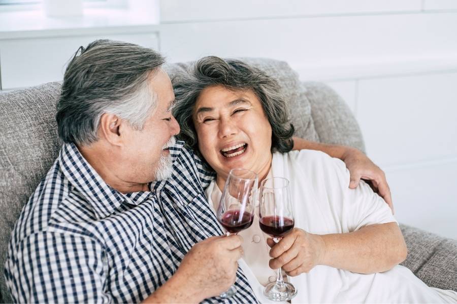 Casal asiático rindo e brindando com uma taça de vinho.
