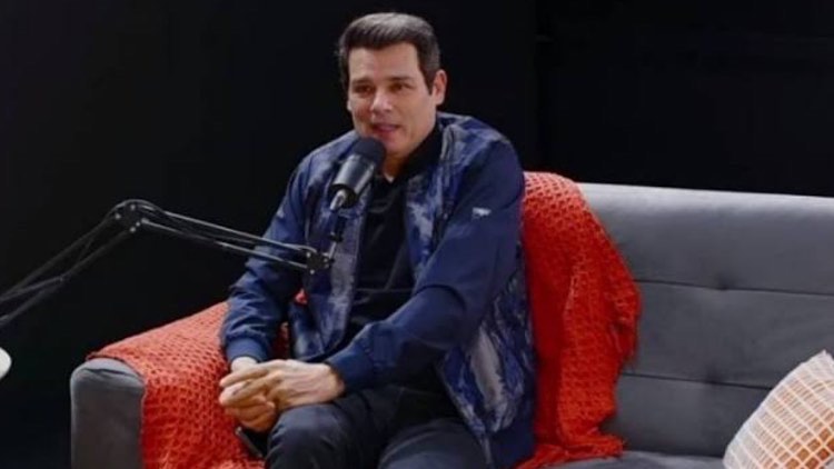 Celso Portiolli de roupa preta falando ao microfone um podcast, sentado no sofá