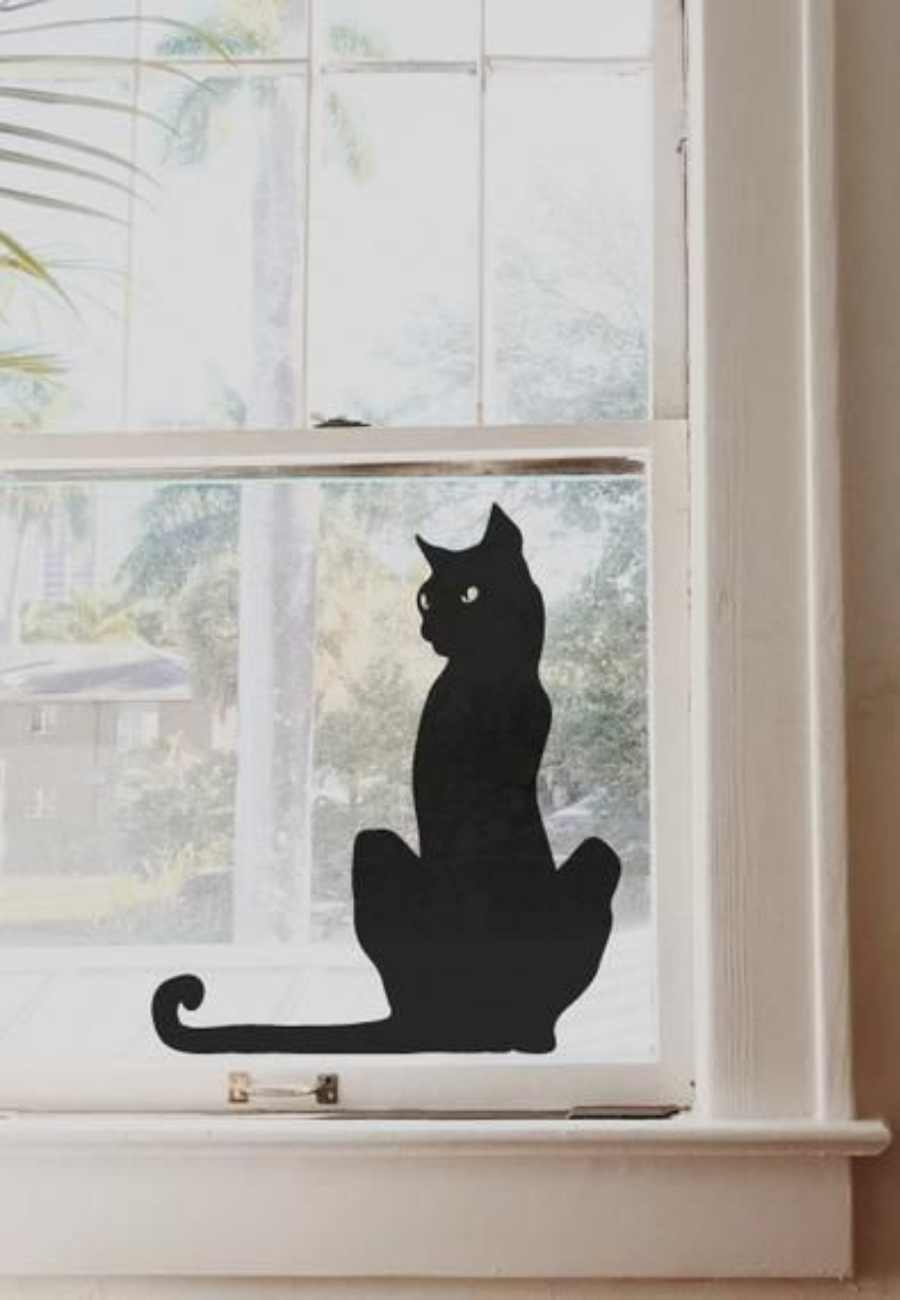 Adesivo de gato preto colado em vidro de janela.