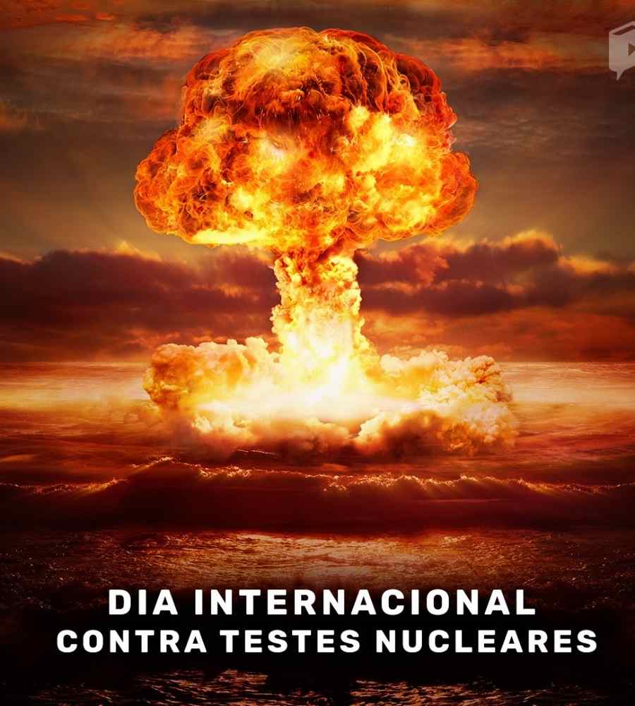 Representação artística de bomba nuclear explodindo em mar. Cores principais da imagem, vermelho, de fogo. Além disso, está escrito "Dia Internacional contra Testes Nucleares" embaixo na imagem. 