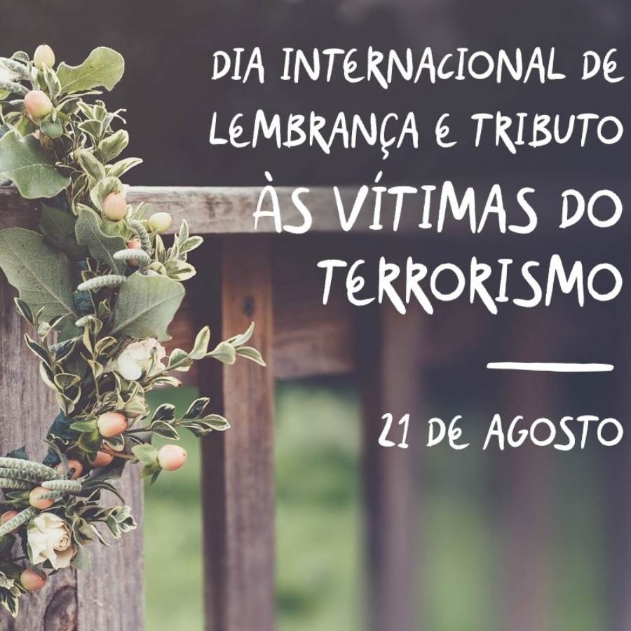 Frase "Dia Internacional de Lembrança e Tributo às vítimas do Terrorismo" escrita em foto de cerca com coroa de flor.