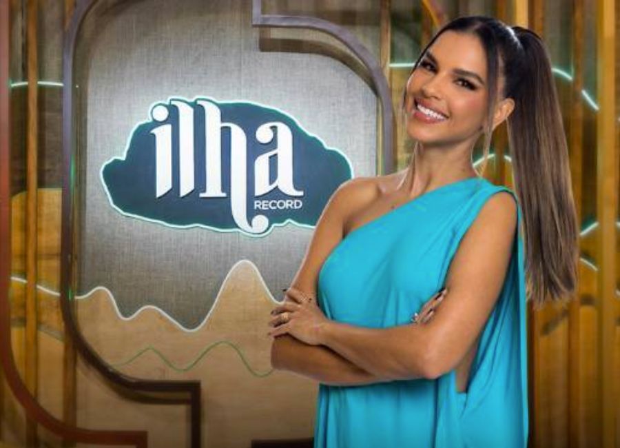 A apresentadora Mariana Rios sorrindo em frente ao letreiro do reality show Ilha Record