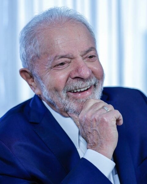 Foto do candidato a presidente Luis Inácio Lula da Silva, sorrindo com a mão apoiada no rosto.
