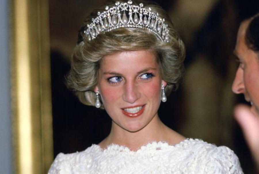 Foto da princesa de Gales de frente usando Lover's Knot Tiara, brincos e vestido branco. Ela está ao lado de seu ex-marido, o príncipe Charles, que aparece de perfil e bem banco no canto da imagem.