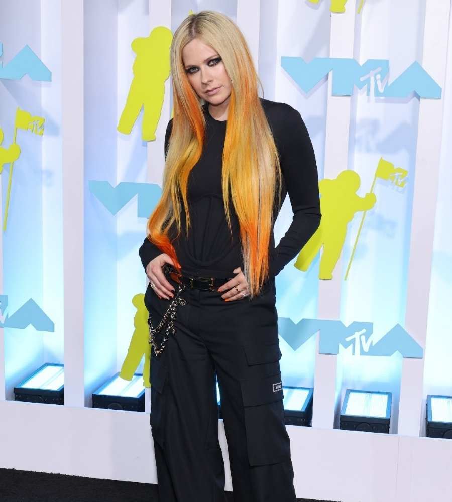Foto de Avril Lavigne no VMA 2022. Ela está toda de preto, com blusa de manga comprida e calça cargo com cinto com correntes. Seu cabelo está loiro com as pontas laranja. 
