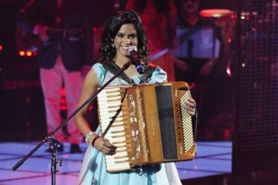 Foto de Lucy Alves no palco do The Voice Brasil. Ela está sorridente e segurando sanfona.