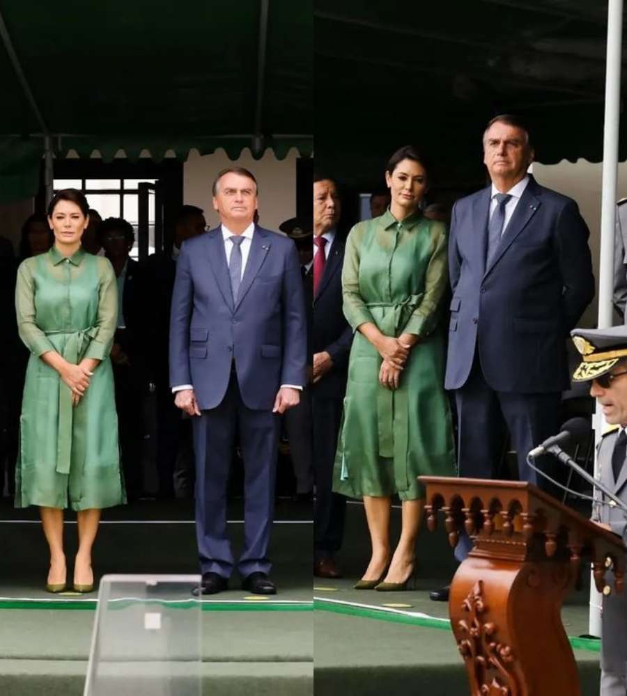 Foto de Michelle Bolsonaro e Bolsonaro  na Cerimônia de Entrega de Espadins aos Cadetes da Turma Dom Pedro II. Os dois estão de pé, rodeados de pessoas. Ela veste roupa verde e ele está de terno.