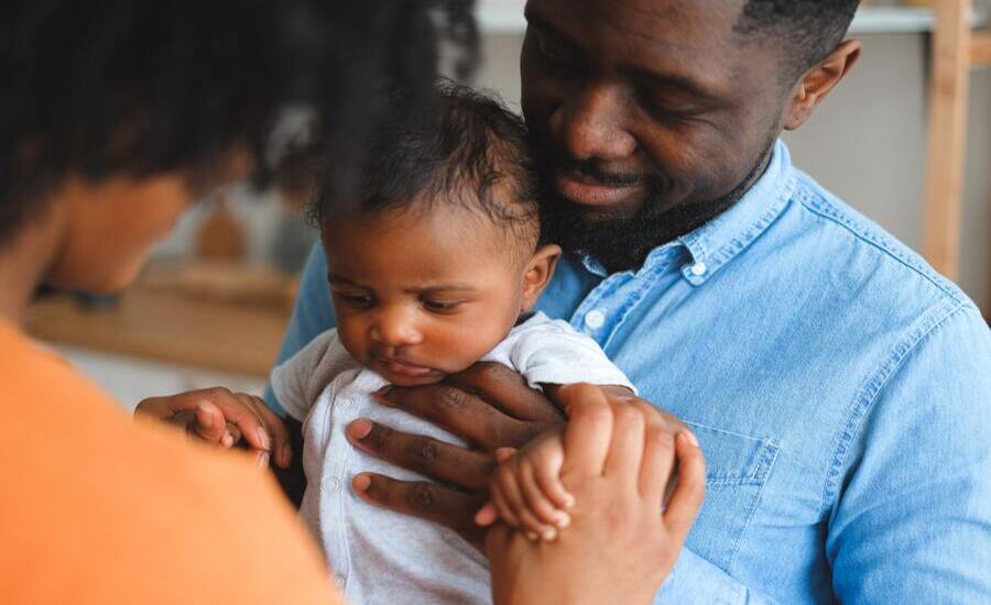 pai negro segurando seu bebê no colo com a mãe segurando suas mãos