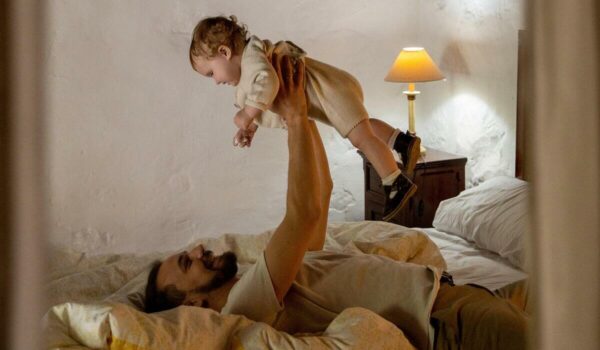 pai deitado na cama segurando um bebê loiro acima de seu corpo