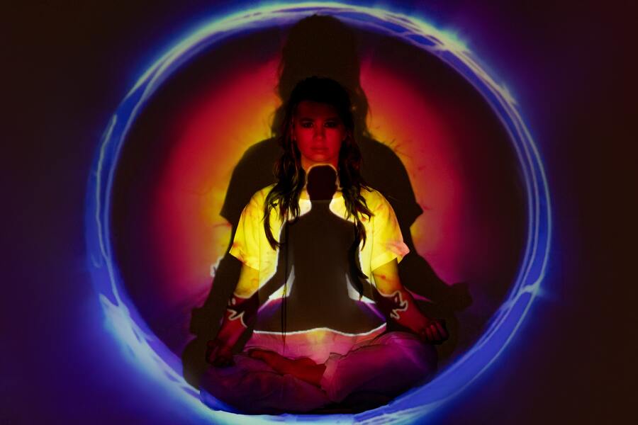 mulher em posição de meditação com diversas cores surgindo