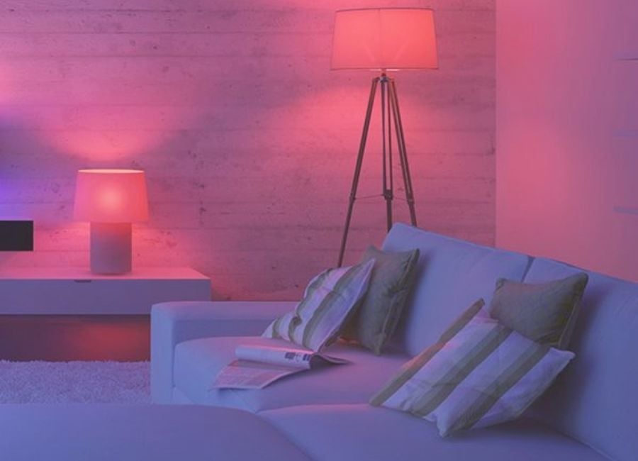 Quarto com uma cama branca, decorada com almofadas também brancas e duas luminárias rosas