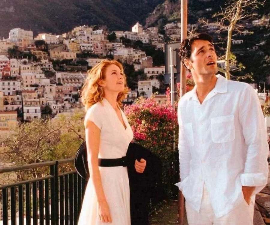 Atores de "Sob o Sol da Toscana" em cena. Os dois estão em pé em ambiente com vista para cidade italiana.