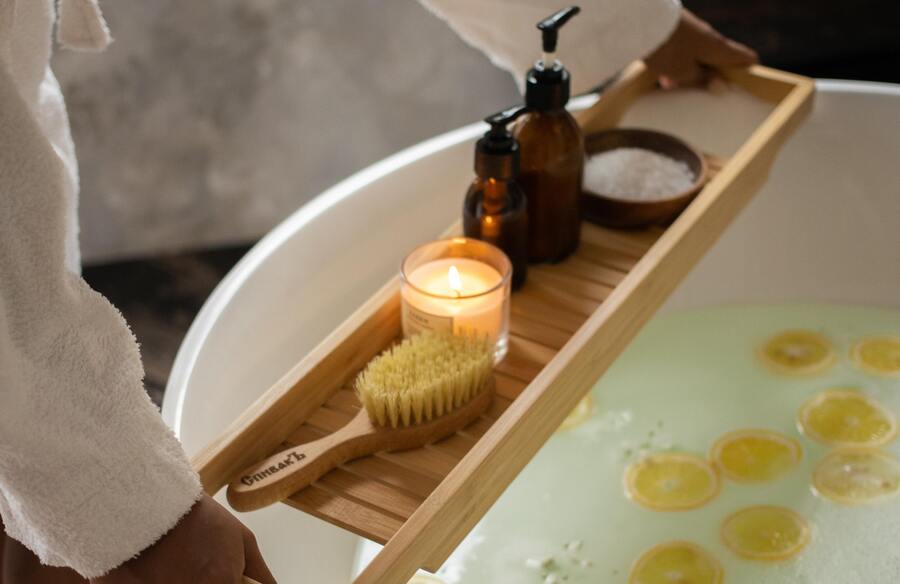 banheira branca com rodelas de laranja e um suporte de madeira segurando vela, sais, uma escova e frascos de sabonete