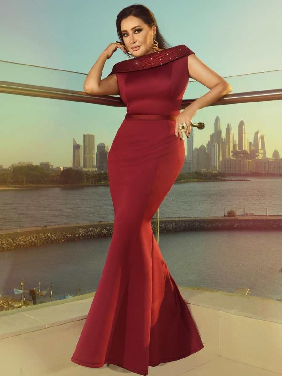 Cantora e atriz árabe Latifa usando vestido da AAVVA. Ela está de pé apoiando os braços em luxuosa cobertura com vista para o mar e arranha-céus.