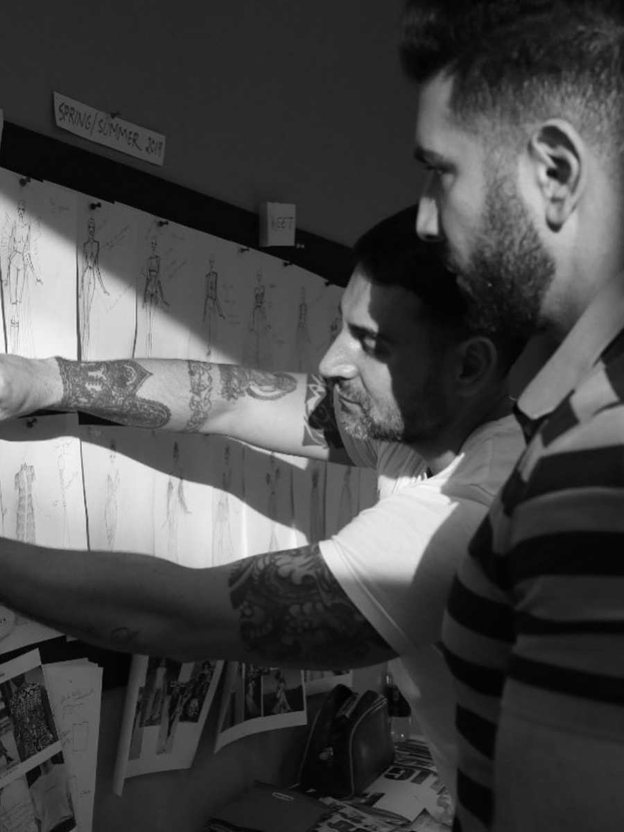 Vincenzo Visciglia e Ahmad Ammar pregando desenhos de peças da coleção Verão 2019 em mural. Foto em preto e branco.