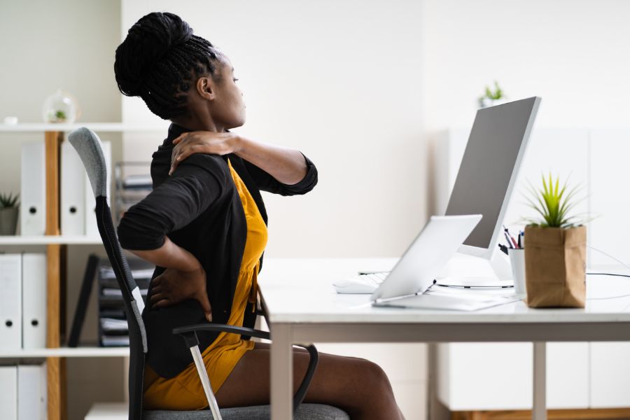 mulher sentada trabalhando em escritório com dor nas costas, consequência do sedentarismo