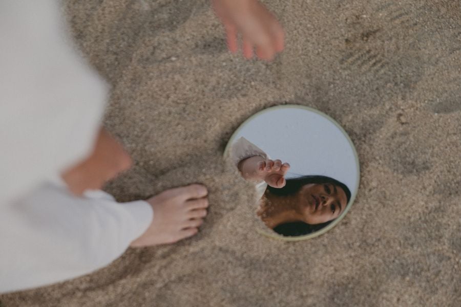 mulher olhando em espelho enterrado na areia, autoconhecimento
