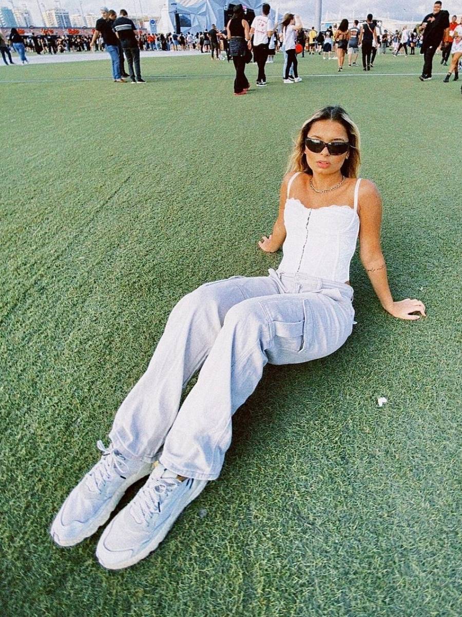 Giovanna Moura sentada na grama do Rock in Rio usando look todo branco