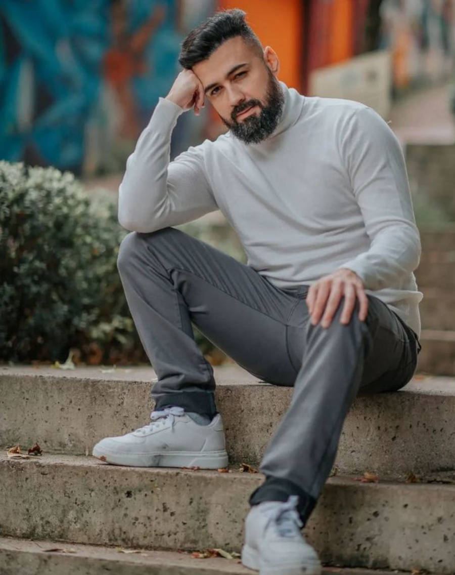 Foto de Bruno Tálamo com blusa branca de gola alta e calça cinza